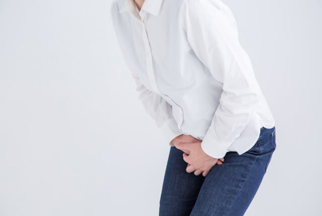 下半身を両手でおさえる女性
